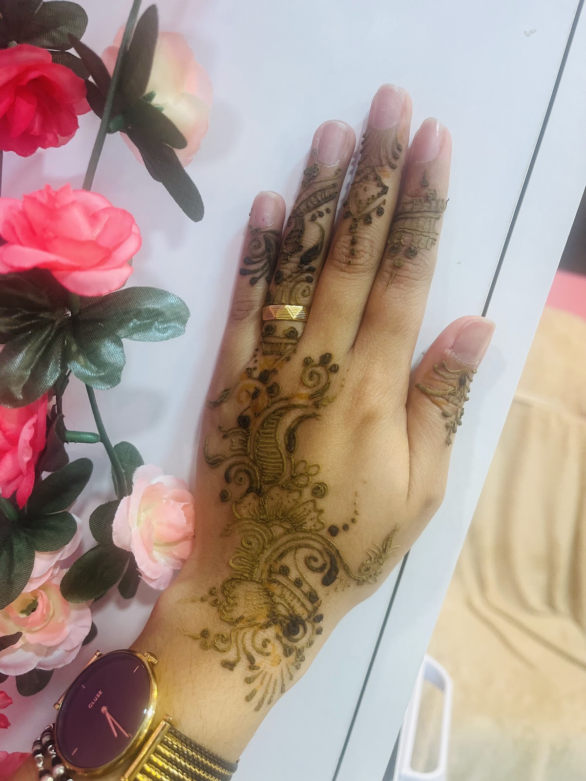 Main décorée de henné doré aux motifs floraux, ongles vernis rose